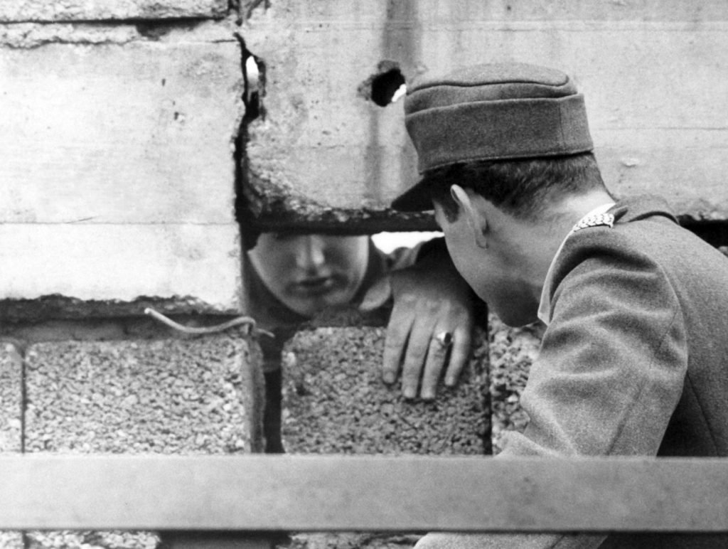 Guards from both sides of Berlin talking through an hole.