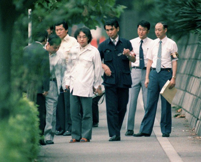 Child killer Tsutomu Miyazaki, wearing glasses at centre left, assists police at a crime scene in 1989.

