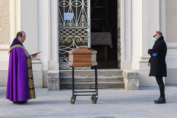  A man wearing a face mask stands by the coffin of his mother as a priest reads prayers during a funeral
Italy passes 100,000 cases 